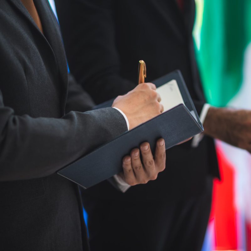 businessmen-signing-agreement-with-flags-in-backgr-2026-01-09-07-54-55-utc (1)